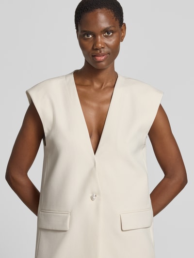 Kobiece model prezentuje kamizelkę 'Weste mit V-Ausschnitt und Pattentaschen' od Copenhagen Muse, mieszanka materiałów z dodatkiem wiskozy, krój regular fit, dekolt w serek, kieszenie z patką, zapięcie na guzik, kolor jasny beż, gładka tekstura, widoczne detale kieszeni, długość tyłu w rozmiarze S: 78 cm, szerokość ramion w rozmiarze S: 46 cm, szerokość w rozmiarze S: 51 cm, widok z przodu, zbliżenie na górną część.