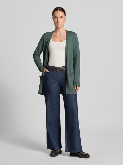 Frauenmodel trägt Strickjacke aus Viskose-Mix von VILA in dunklem Grün, taillierte Passform, seitliche Eingrifftaschen, Ganzkörperansicht von vorne.