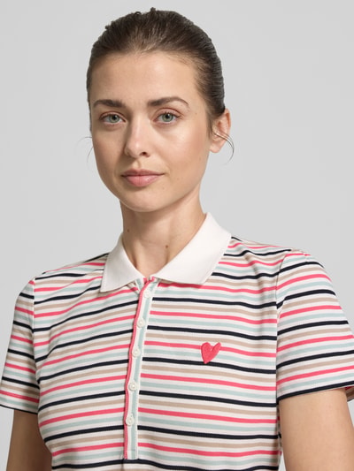 Modelka kobieca nosi Regular Fit Poloshirt aus Baumwoll-Mix von Tom Tailor, efekt: wzór w paski na całej powierzchni, wyhaftowany motyw, kołnierzyk polo, dekolt w serek, listwa guzikowa, krótki rękaw, wykończenie materiału: pika, mieszanka bawełny, ujęcie: zbliżenie na górną część ciała.