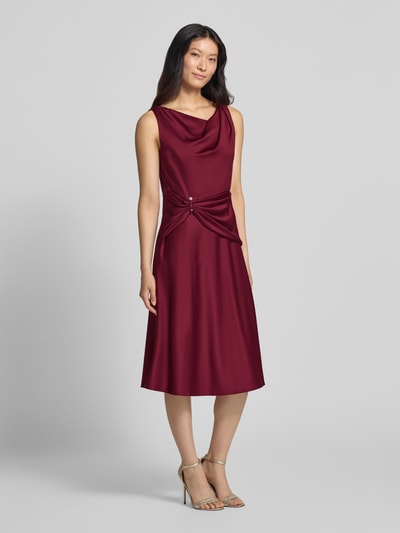 Frauenmodel trägt Cocktailkleid aus Satin mit Raffungen von Adrianna Papell in Bordeaux mit taillierter Passform, Ganzkörperansicht von vorne.