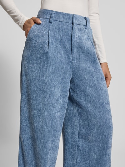 Frauenmodel trägt Wide Fit Stoffhose in Denim-Optik Modell 'Zvally' von Gestuz, Bundfalten, Gesäßtasche, Nahaufnahme Oberkörper.