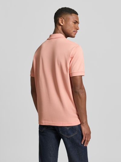Männermodel trägt Regular Fit Poloshirt aus Baumwoll-Mix von Lacoste in Uni-Rosa, Piqué-Struktur, Logo-Detail, Ganzkörperansicht Rückansicht.