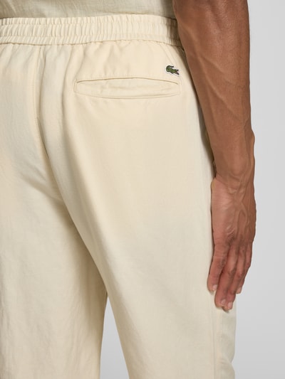 Männermodel trägt Straight Leg Stoffhose aus Leinen-Mix von Lacoste in Beige mit Label Patch, elastischem Bund, Detailaufnahme Rückansicht.