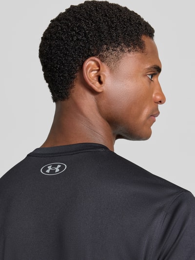 Männermodel trägt schwarzes Regular Fit Sport-T-Shirt mit Label-Print von Under Armour, glatte Textur, Nahaufnahme Oberkörper.