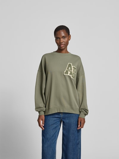 Frauenmodel trägt Relaxed Fit T-Shirt mit Logo-Print von Anine Bing aus reiner Baumwolle in Olivgrün, Rundhalsausschnitt, eingefasste Ärmelabschlüsse, Rückenlänge 60 cm, Ganzkörperansicht von vorne.