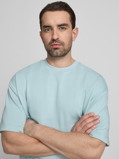 Männermodel trägt Oversized T-Shirt mit Rundhalsausschnitt von Lindbergh in Hellblau, Baumwoll-Mix, Label-Detail, Nahaufnahme Oberkörper.