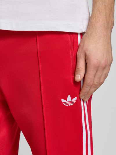 Männermodel trägt rote Sweatpants mit elastischem Bund von adidas Originals, weiße Streifen, Baumwoll-Mix, Nahaufnahme Oberschenkel.