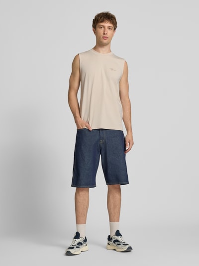 Männermodel trägt Tanktop mit Label-Stitching und Rundhalsausschnitt von Pegador in Beige, Relaxed Fit, reine Baumwolle, Ganzkörperansicht von vorne.