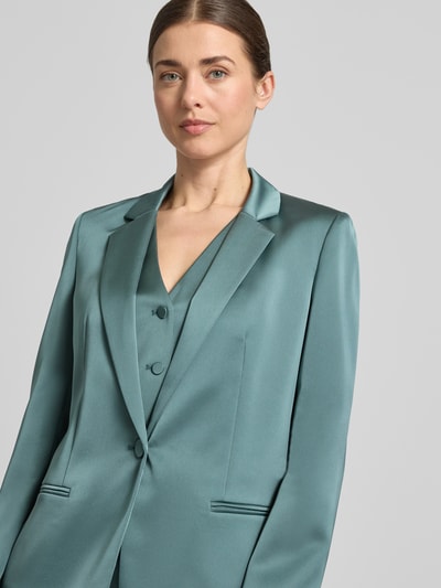 Vrouwenmodel draagt Slim Fit Blazer mit Paspeltaschen van Jake*s Cocktail in satijnen turquoise, met reverskraag en knoopsluiting, borst- en paspelzakken, ruglengte maat 36: 65 cm, detailopname bovenlichaam.