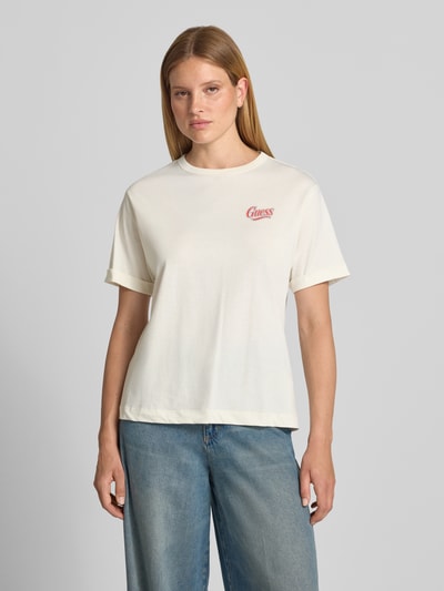 Frauenmodel trägt Relaxed Fit T-Shirt mit Ziersteinbesatz Modell 'Emotional' von GUESS, cremefarben, reine Baumwolle, Ganzkörperansicht von vorne.