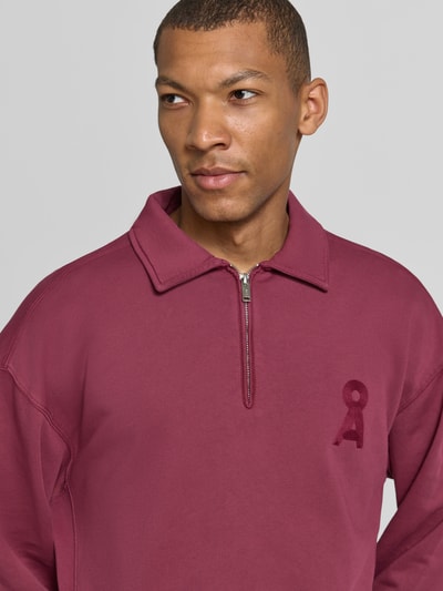 Männermodel trägt bordeauxroten Relaxed Fit Troyer aus reiner Baumwolle Modell 'ICONIC Å GMT' von ARMEDANGELS, Nahaufnahme Oberkörper.