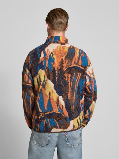 Männermodel trägt Fleecepullover mit Label-Patch Modell 'HELVETIA' von Columbia in buntem Muster, Ganzkörperansicht Rückansicht. Gerader Schnitt, Stehkragen, Herrenmodell, strukturierte Fleece-Textur.