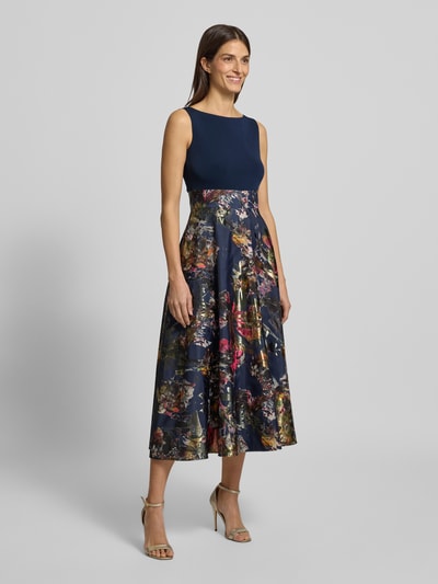 Frauenmodel trägt Abendkleid mit U-Boot-Ausschnitt von Christian Berg Cocktail im Material-Mix mit Stretch-Anteil, taillierter Schnitt, blickdichter Unterrock, Nahtreißverschluss, Rückenlänge bei Größe 36: 123 cm, Brustweite bei Größe 36: 41 cm, florales Muster in Blau und Bunt, Ganzkörperansicht von vorne.
