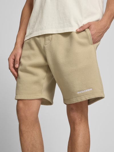Männermodel trägt Shorts mit elastischem Bund und Logo-Stitching von Pegador, Beige, Baumwoll-Mix, Loose-Fit, Nahaufnahme Oberkörper. Bundweite 38 cm, Innenbeinlänge 23 cm, französische Eingrifftaschen.
