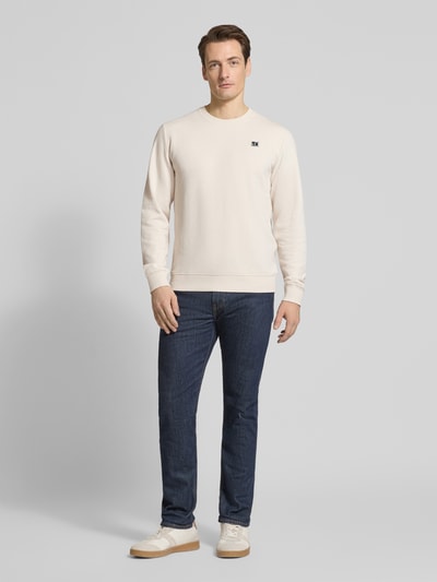 Męski model nosi Regular Fit Sweatshirt aus Baumwoll-Mix von s.Oliver RED LABEL, jednolity kolor, wyhaftowane logo, krój regular fit, okrągły dekolt, długi rękaw, prążkowane wykończenia, dzianina dresowa, mieszanka bawełny, całkowity widok z przodu.