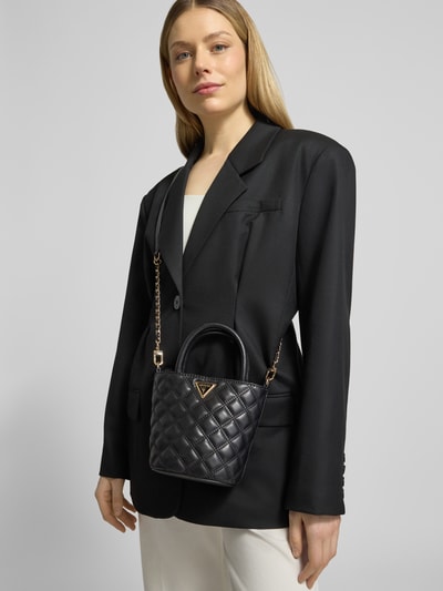 Frauenmodel trägt schwarze Handtasche mit Steppnähten Modell 'GIULLY II' von Guess, glänzende Oberfläche, Nahaufnahme Oberkörper. Label-Applikation, Tragehenkel, Schulterriemen, Maße und Details gemäß Kontext.