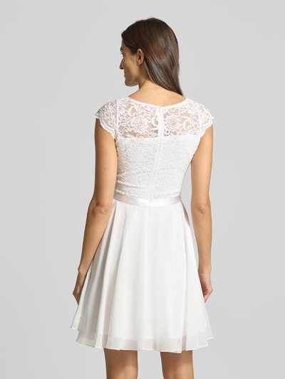 Frauenmodel trägt Cocktailkleid mit Spitzenbesatz und Bindegürtel von SWING, weißer Material-Mix mit Stretch-Anteil, A-Linie, Minikleid, Rückansicht.