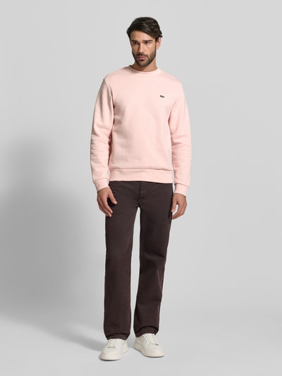 Mannelijk model draagt Classic Fit Sweatshirt uit katoenmix van Lacoste in effen lichtroze met logo-stitching, geribde boorden, lange mouwen, ronde hals; volledige lichaamsaanzicht van voren.