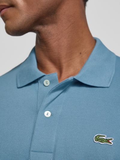 Mężczyznamodel nosi koszulkę polo Regular Fit Poloshirt aus reiner Baumwolle model 'CORE' od Lacoste w niebieskim kolorze, tekstura pikowana, zbliżenie na górną część ciała, kontekst: koszulka polo męska od Lacoste.