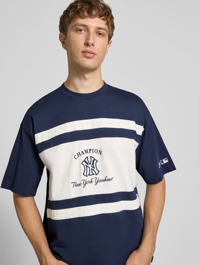 Männermodel trägt Relaxed Fit T-Shirt aus reiner Baumwolle von Champion, navy-weiß mit Logo-Print, Nahaufnahme Oberkörper