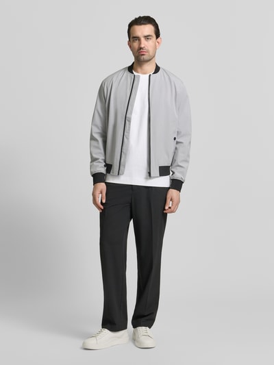 Männermodel trägt Regular Fit Bomberjacke mit Stehkragen von MCNEAL in Hellgrau mit schwarzen Bündchen, Eingrifftaschen und Reißverschluss, Ganzkörperansicht von vorne.