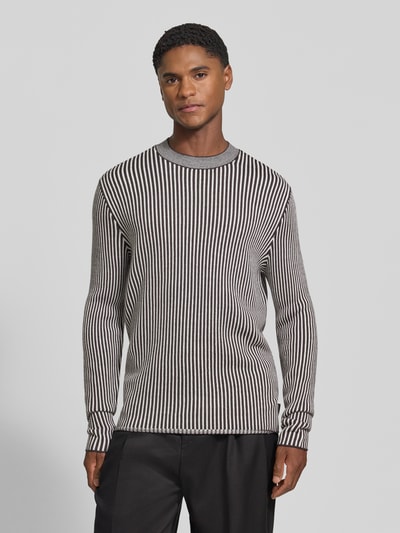 Mannelijk model draagt Regular Fit gebreide pullover uit scheerwolmix met streepmotief van Armani Exchange, zwarte en grijze tinten, elastische boordjes, ruglengte maat M 70 cm, mouwlengte maat M 69 cm, herenmodel, voorkant volledige lichaamsweergave.