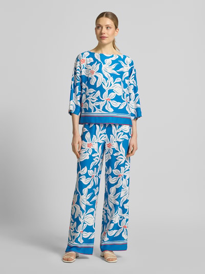 Vrouwenmodel draagt stoffen broek van viscose model 'Rylie' van GUIDO MARIA KRETSCHMER WOMAN, relaxed fit, all-over look, elastische band, bandwijdte maat 36: 36 cm, binnenbeenlengte maat 36: 77 cm, blauw met groot wit bloemmotief, gladde textuur. Volledig vooraanzicht.