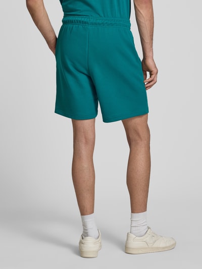 Männermodel trägt Sweatshorts mit Logo und elastischem Bund von CHAMPION in Türkis, Baumwoll-Mix, Regular Fit, Rückansicht Ganzkörperansicht.