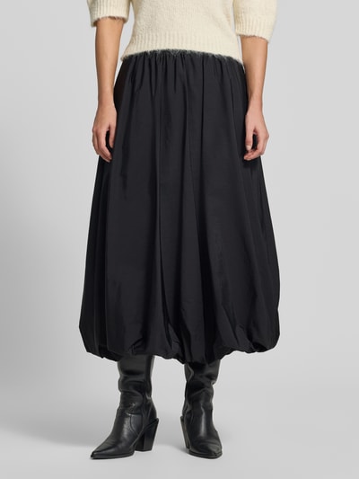 Männermodel trägt Ausgestellter Midi-Rock mit Tunnelzug Modell 'CIURMA' von Weekend Max Mara in Schwarz mit matter Textur, Ganzkörperansicht von vorne.