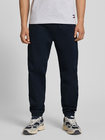 Männermodel trägt Straight Fit Jeans aus reiner Baumwolle van Tommy Jeans in donkerblauw denim met 5-pocket-design en elastische taille en pijpen, loose straight fit, voorkant detailopname