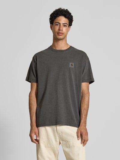 Männermodel trägt Herren T-Shirt mit Label-Detail Modell 'Nelson' von Carhartt Work In Progress aus Reine Baumwolle, Relaxed-Fit, Rundhalsausschnitt, Rückenlänge bei Größe M 72 cm, Dunkelgrau mit glatter Struktur, Ganzkörperansicht von vorne.