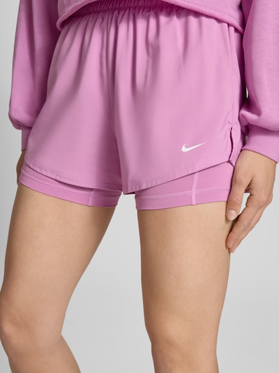 Frauenmodel trägt Shorts im 2-in-1-Look mit Logo von NIKE TRAINING in Rosa, elastischer Bund, Material-Mix mit Stretch-Anteil, Nahaufnahme Oberschenkel.