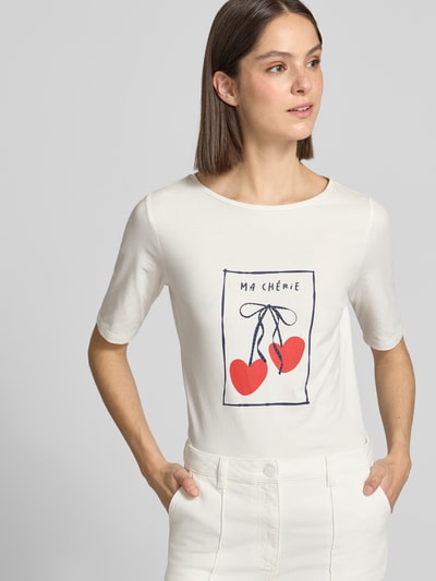 Modelka nosi damski t-shirt z nadrukiem z motywem od More & More, mieszanka bawełny i elastanu, krój regular fit, okrągły dekolt, długość tyłu w rozmiarze 36: 60 cm, jasne kolory z czerwonym motywem, gładka faktura. Ujęcie: z przodu, od pasa w górę.