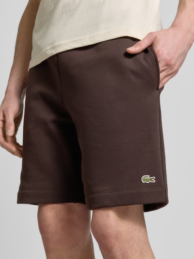 Männermodel trägt Regular Fit Sweatshorts aus Baumwoll-Mix von Lacoste in Braun, unifarben, Label Patch, Nahaufnahme Oberschenkel.