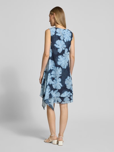 Vrouwenmodel draagt cocktailjurk im allover-look aus fließendem stoff van Christian Berg Cocktail in blauwe tinten met bloemvormen, rugaanzicht, context: dames cocktailjurk van Christian Berg Cocktail, chiffon, a-lijn, mini-jurk, all-over look, vloeiende stof, cascadehals, ruglengte bij maat 36: 36 cm, borstwijdte bij maat 36: 44 cm.