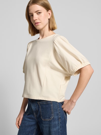 Frauenmodel trägt Relaxed Fit Sweatshirt mit Rundhalsausschnitt Modell 'Aurati' von Drykorn, hellbeiger Baumwoll-Mix, Halbarm, elastische Ärmelabschlüsse, glatte Textur, kombiniert mit blauer Jeans, Ganzkörperansicht von vorne.