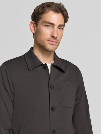 Męski model nosi Slim Fit Hemdjacke mit Viskose-Anteil od Lindbergh, elastyczna mieszanka materiałów, wykładany kołnierz, listwa guzikowa na całej długości, nakładana brustasza, wpuszczane kieszenie, długość tyłu w rozmiarze M: 70 cm, ciemnoszara, tekstura gładka, prosty fason, widok na górną część ciała z przodu.
