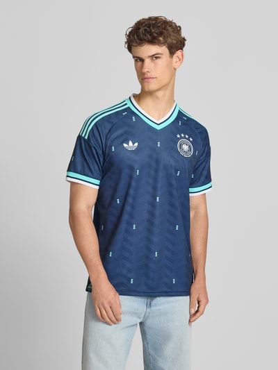 Männermodel trägt DFB Auswärtstrikot Deutschland 2026 von adidas Sportswear, Mehrfarbig, Optik, Slim-Fit, Logo-Applikation, V-Ausschnitt, Ärmelform: Kurzarm, Ganzkörperansicht von vorne.