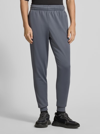 Męski model nosi Sweatpants mit elastischem Bund od Under Armour, kolor szary, luźny krój, kieszenie, widok całej sylwetki z przodu.