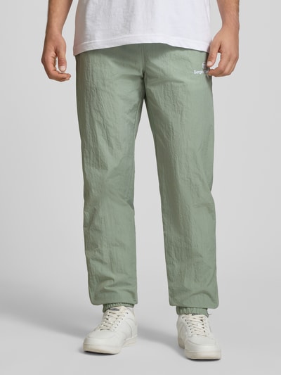 Männermodel trägt Straight Fit Stoffhose mit Logo-Stitching Modell 'Nayla' von SERGIO TACCHINI in Hellgrün, leichte Struktur, elastischer Bund mit Tunnelzug, elastische Beinabschlüsse, Innenbeinlänge 77 cm bei Größe M, Ganzkörperansicht von vorne.