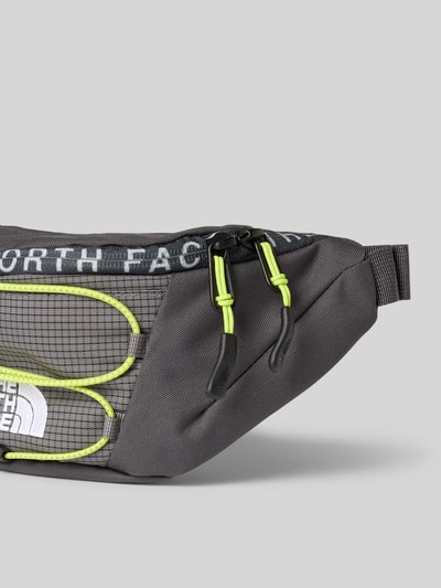 Produktfoto, graue Bauchtasche mit Label-Stitching Modell 'JESTER LUMBAR' von The North Face, gelbe Akzente, Reißverschluss, detailreiche Textur, größenverstellbar, Maße 26x17x10 cm, 50 cm Schulterriemen.