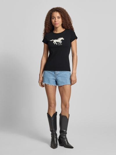Kobiece modelka nosi Regular Fit T-Shirt mit Logo-Print Modell 'Loa' od Mustang, czarny, bawełna, krótki rękaw, dekolt okrągły, przód, całe ciało