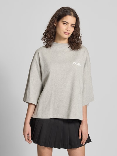 Kobiece model nosi Oversized T-Shirt mit Rundhalsausschnitt od Karo Kauer, bawełna, krój oversized, krój krótki, nadruk z logo, okrągły dekolt, długość tyłu w rozmiarze S: 61 cm, przód, ujęcie całej sylwetki.