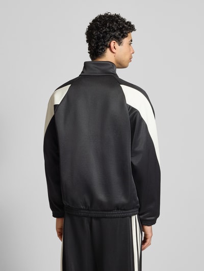 Męski model nosi Kurtkę treningową z logo i stójką od adidas Sportswear, mieszanka materiałów z bawełną, krój regular fit, długość tyłu 68 cm, długość rękawa 67 cm, kolor czarno-biały, widok całej sylwetki z tyłu.