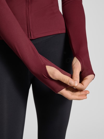 Vrouwenmodel draagt Slim Fit Sweatjacke met Stehkragen Modell 'Yoga' van Gina Tricot, bordeauxrood, elastisch materiaal, detailopname handen.