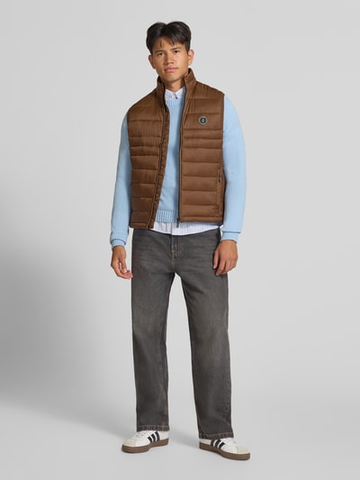 Mannenmodel draagt bodywarmer met ritssluitingszakken Model 'KINGSLEY' van JACK & JONES in bruin, regular fit, opstaande kraag, volledig beeld van voren. Ruglengte maat M: 65 cm, schouderbreedte: 42 cm, borstwijdte: 43 cm.