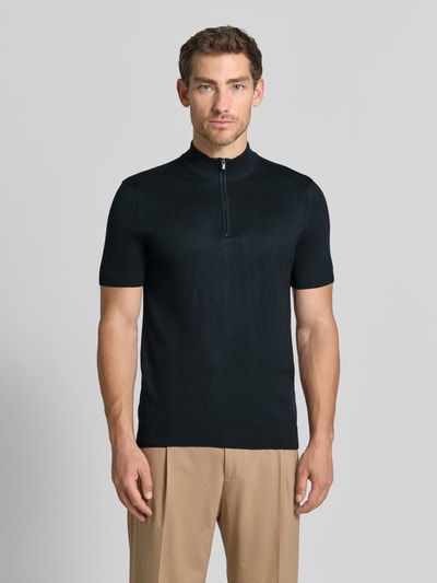 Männermodel trägt Strickshirt aus Viskose-Mix mit Stehkragen Modell 'Vadin' von JOOP!, Schwarz, Reißverschluss, Ganzkörperansicht von vorne. Körpernaher Schnitt mit kurzem Arm, Rückenlänge 68 cm, Ärmellänge 24 cm.