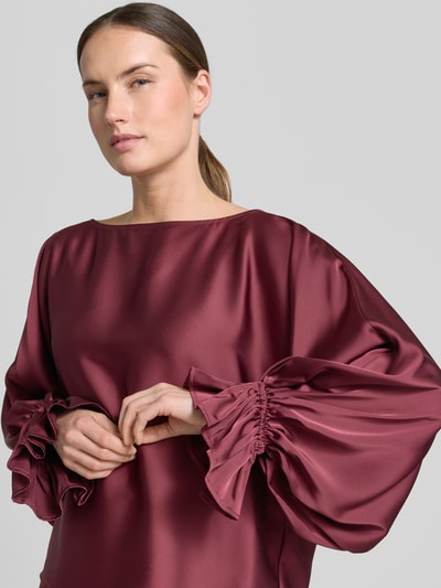 Frauenmodel trägt Blusenshirt aus Satin mit Rundhalsausschnitt von V by Vera Mont in Weinrot mit Trompetenärmeln, Nahaufnahme Oberkörper. Regular Fit, glatte glänzende Textur, Rückenlänge 58 cm, Ärmellänge 63 cm.