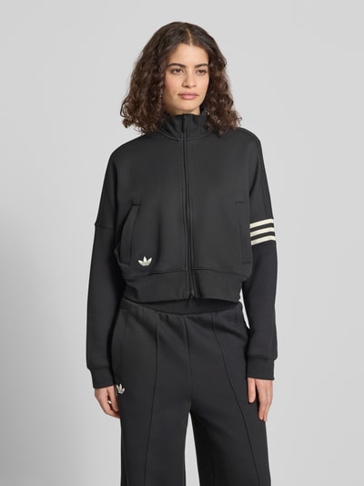 Kobiece modelka nosi Regular Fit Sweatjacke aus Baumwoll-Mix von adidas Originals, czarny, jednolity, logo haft, zamek błyskawiczny, stojący kołnierz, długie rękawy, ściągacze, kieszenie boczne, materiał typu sweat, mieszanka bawełny, całkowity widok z przodu.