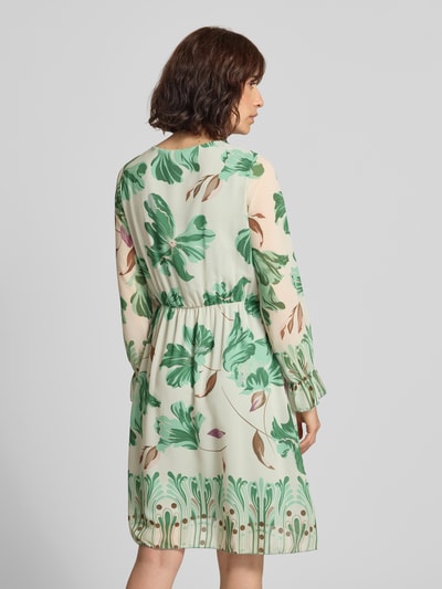 Frauenmodel trägt Knielanges Kleid im Allover-Look Modell 'Ja44milaa' von ZABAIONE, grün-beige mit floralen Mustern, Chiffon, Ganzkörperansicht Rückansicht.